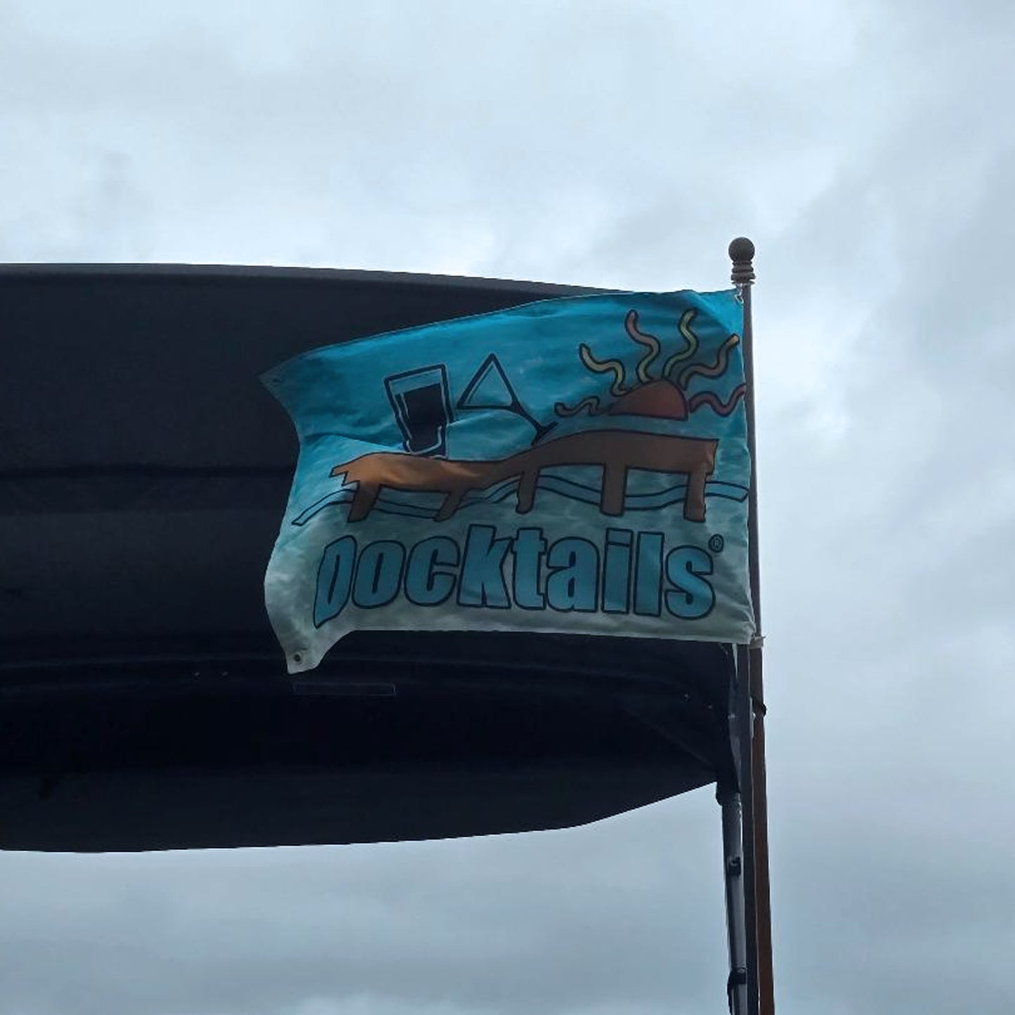 Boat flag showing Docktails text with graphic of a dock, pint glass, sideways martini glass and a sun