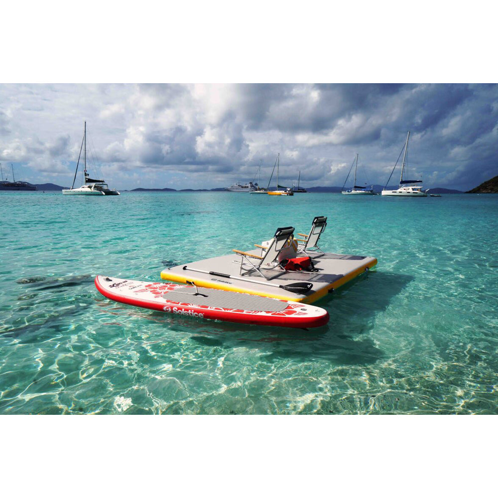 Solstice inflatable dock in the ocean holding beach chairs and with a paddleboard tied to it