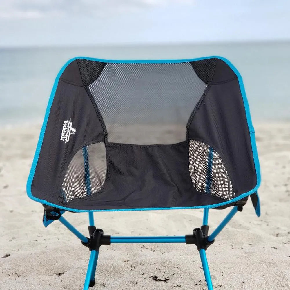 A blue and black mesh beach chair with a white 'Docktails' logo, set on a sandy beach with the ocean in the background.