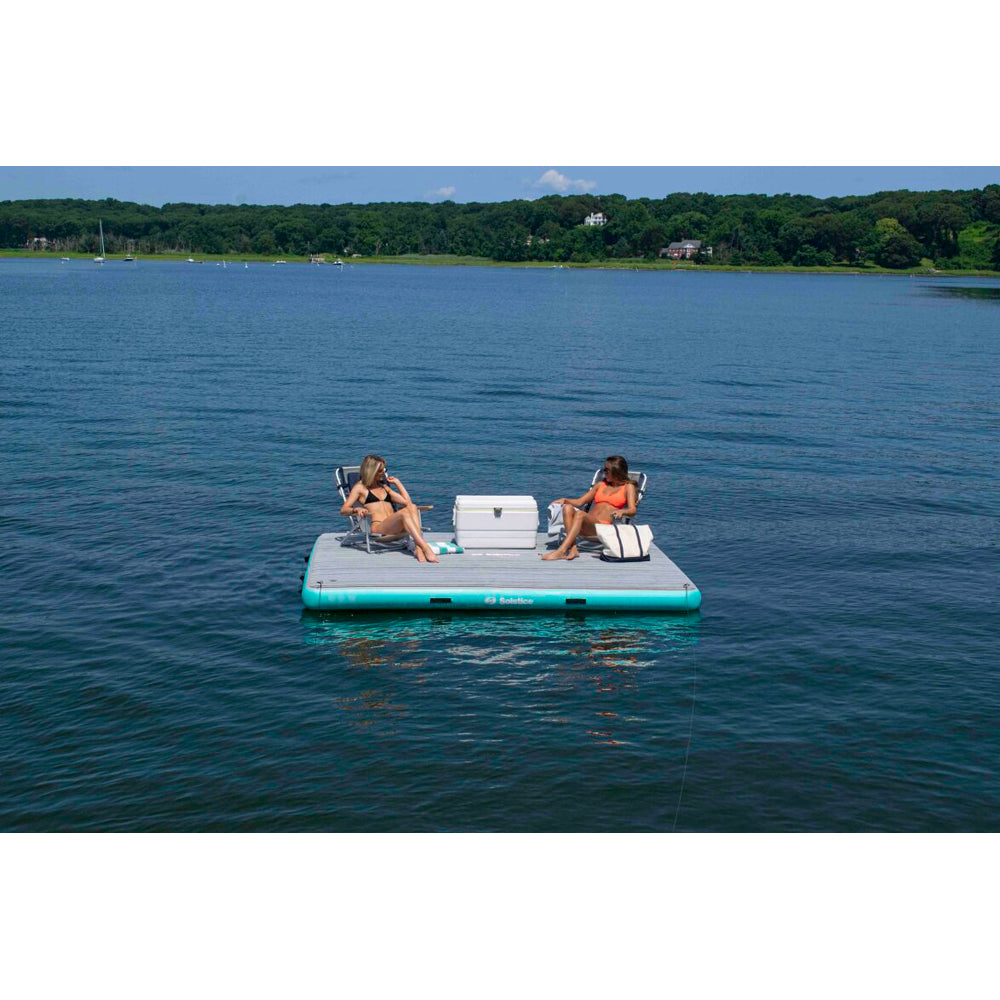 Solstice inflatable dock with integrated traction pad, shown holding two people in beach chairs and a cooler