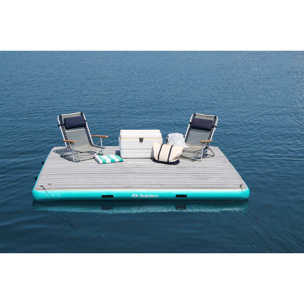 Solstice inflatable dock with integrated traction pad, shown holding two beach chairs and a cooler