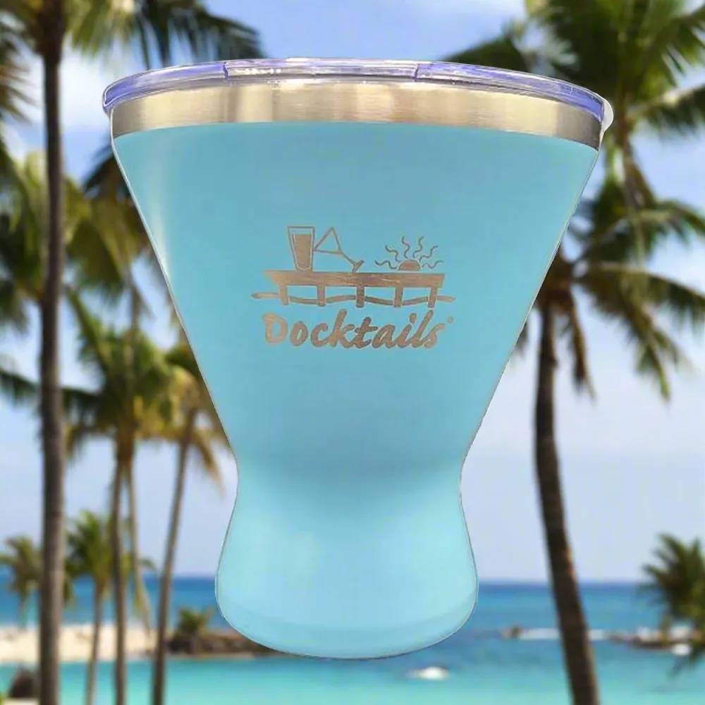 A light blue insulated tumbler with a clear lid and an engraved 'Docktails' logo, shown against a blurred tropical beach background with palm trees and ocean.