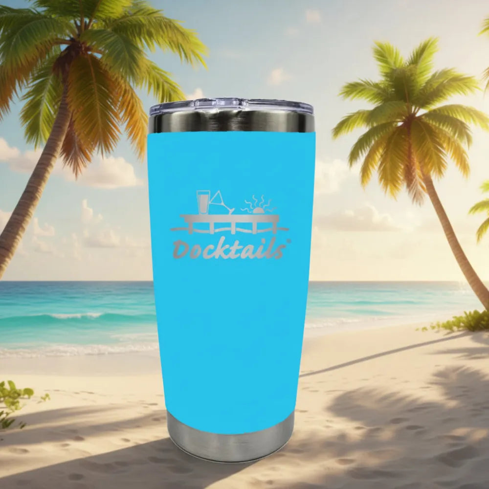 A bright blue insulated travel tumbler with a stainless steel lid and base, featuring an engraved graphic of a dock with a sun above it and a martini glass and pint glass on top of it, with the word 'Docktails' engraved on the front. The background shows a beach scene with palm trees and aqua-colored ocean.